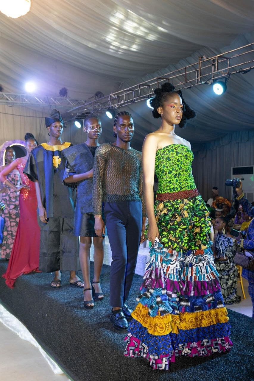 Models walk a runway showcasing vibrant, multi-colored tiered dresses and contemporary African-inspired fashion designs.